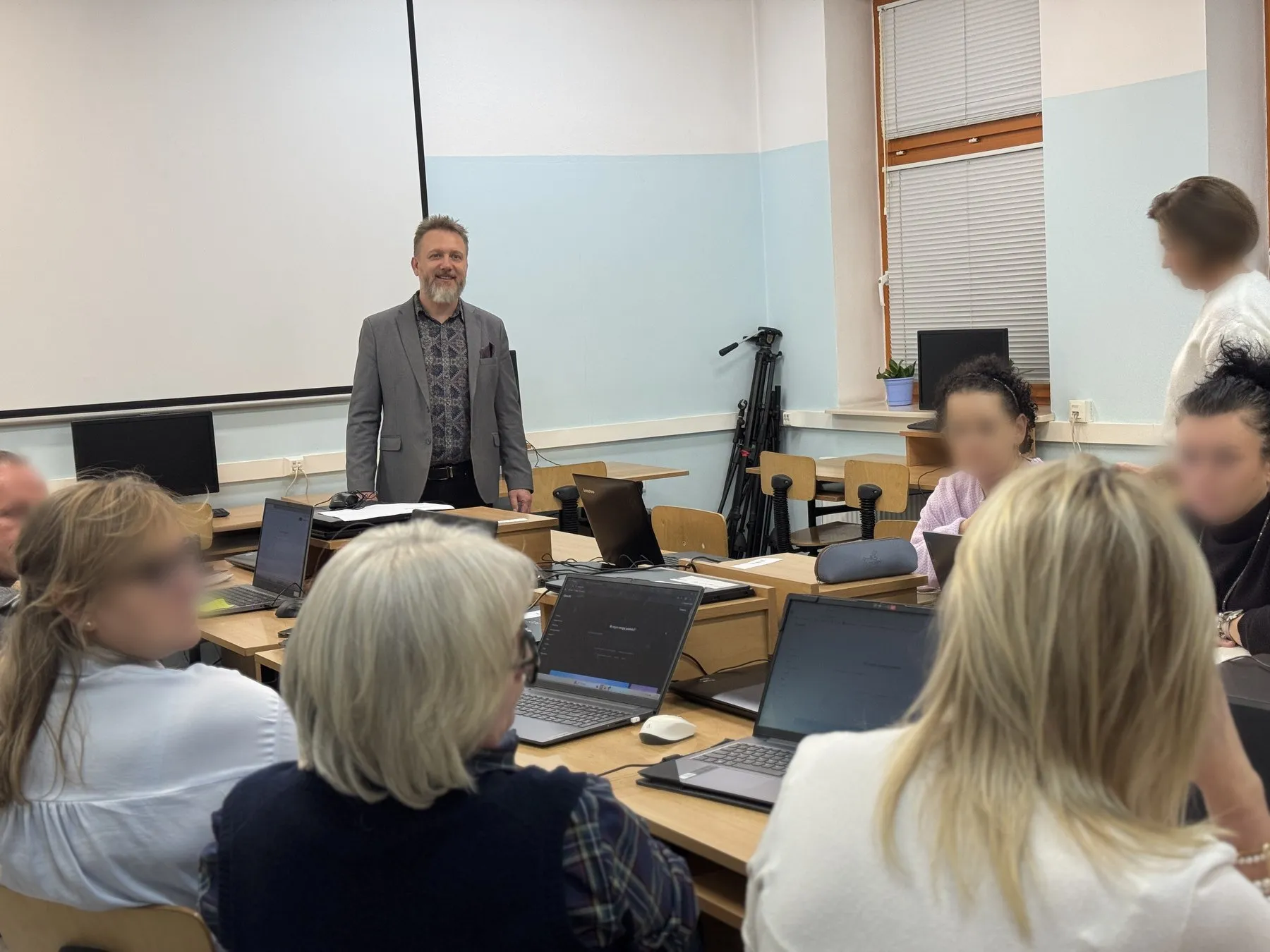 Uczestniczki szkolenia z otwartymi laptopami w sali wykładowej; prowadzący stoi przy pierwszym rzędzie