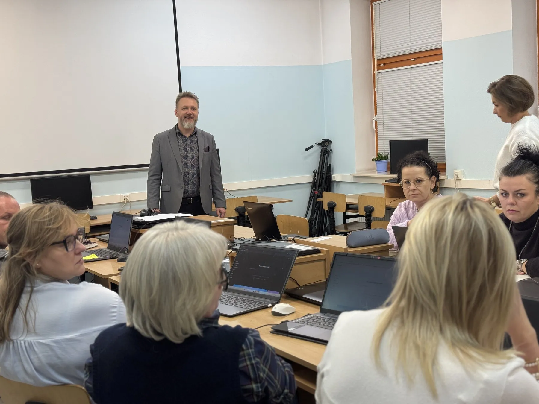 Uczestniczki szkolenia z otwartymi laptopami w sali wykładowej; prowadzący stoi przy pierwszym rzędzie
