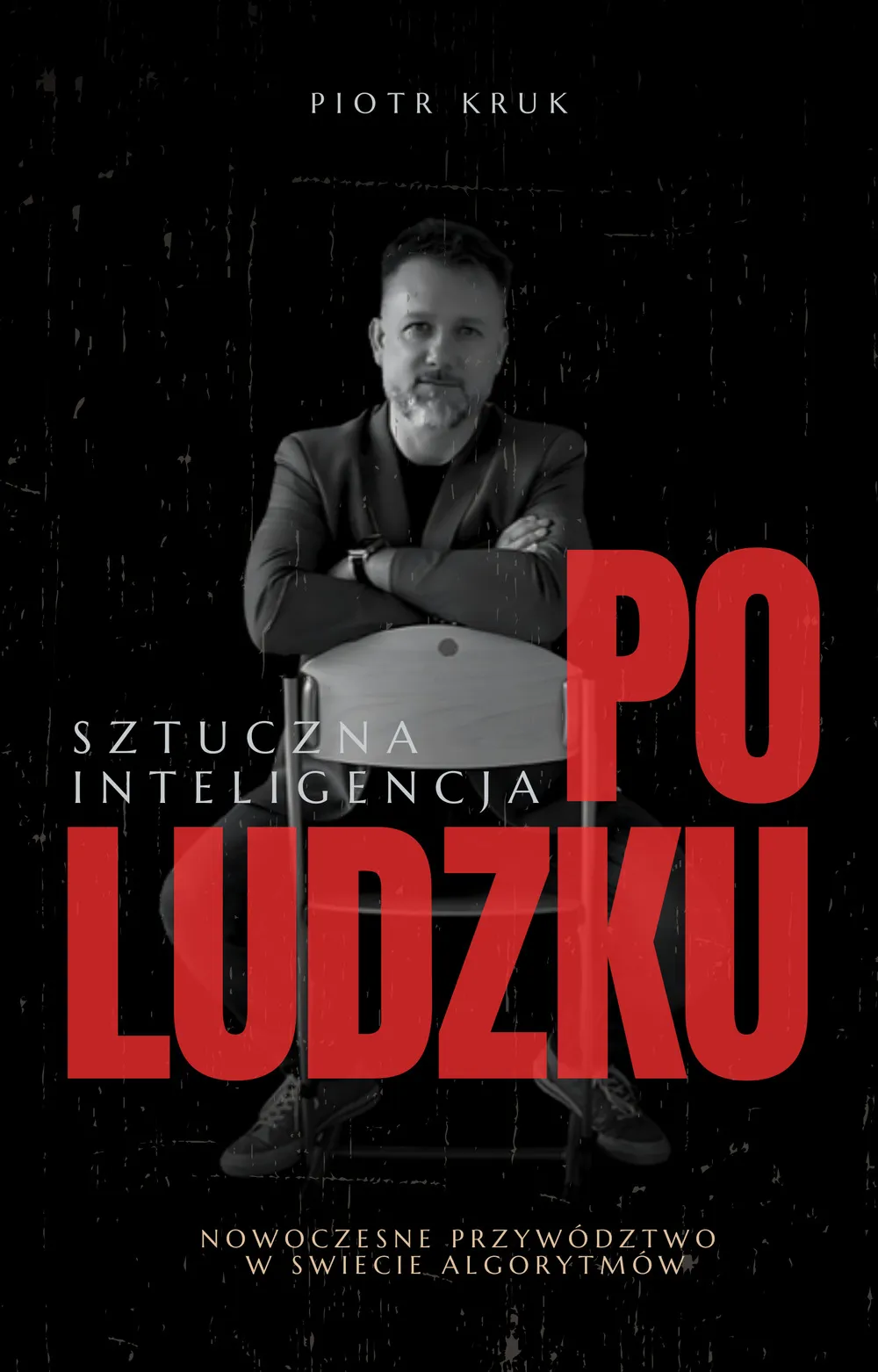Okładka e-booka „Sztuczna inteligencja po ludzku” — Piotr Kruk siedzi okrakiem na krześle na czarnym tle, tytuł złożony czerwonymi wersalikami