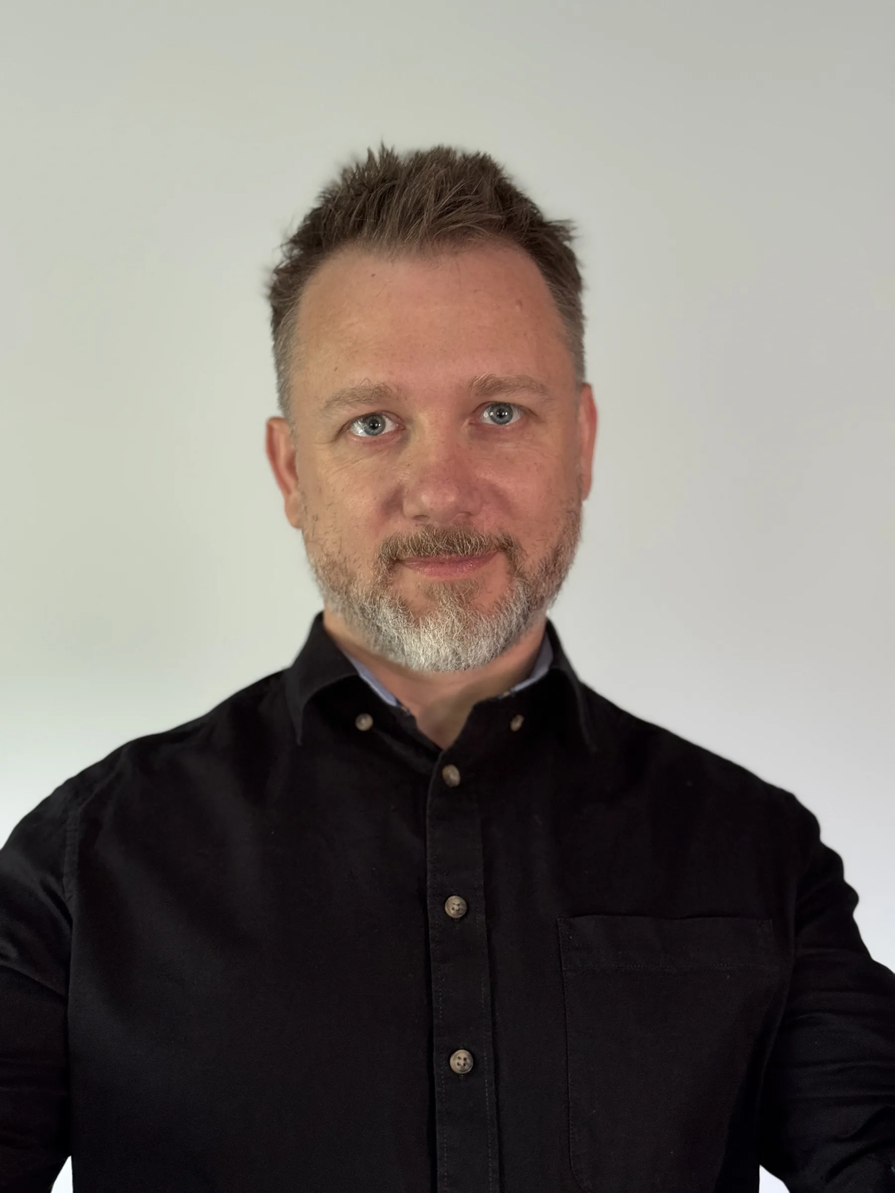 Piotr Kruk — portret na jasnym tle, w ciemnej koszuli