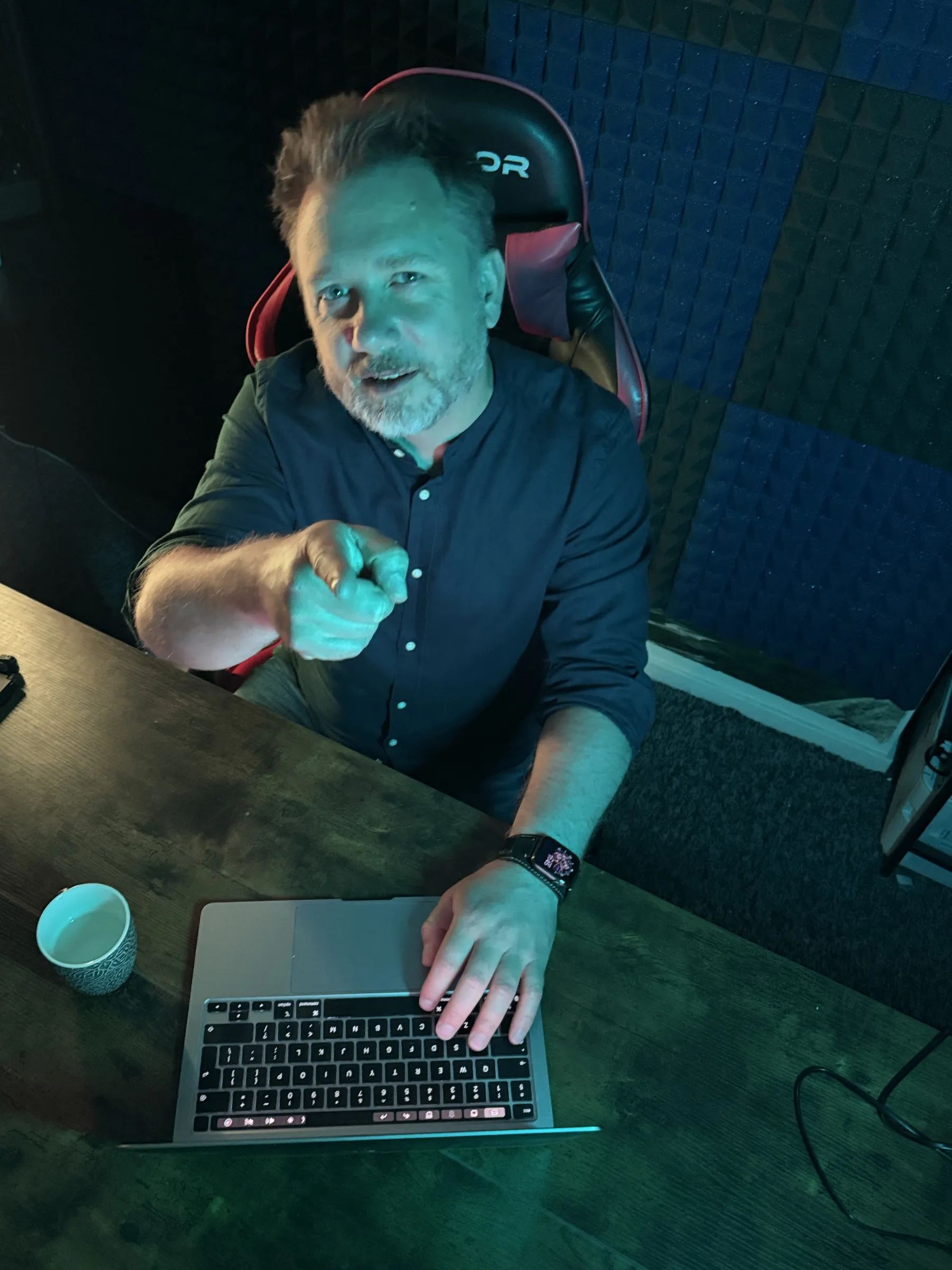 Piotr Kruk przy biurku w ciemnym studiu, przed laptopem
