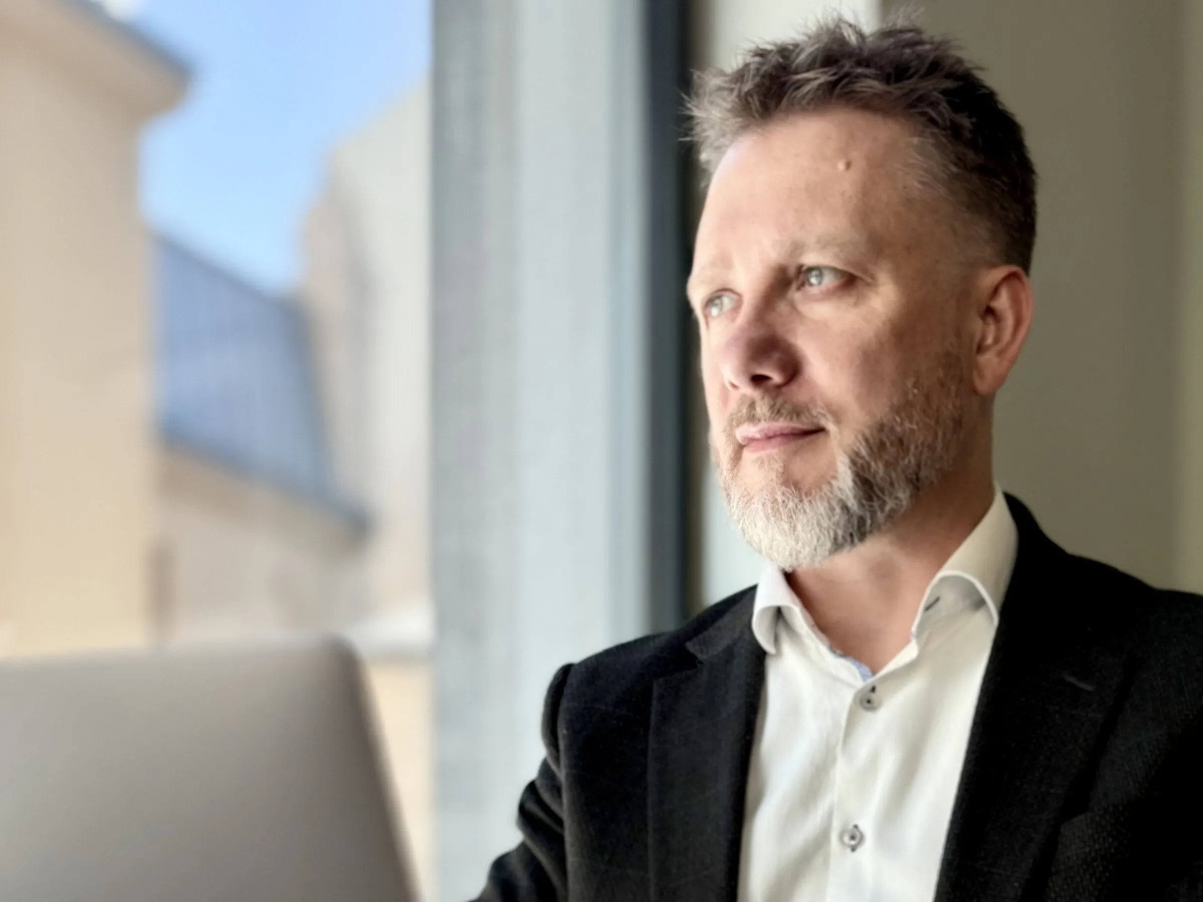 Piotr Kruk siedzi przy laptopie w kawiarni i patrzy w stronę okna ponad otwartym ekranem