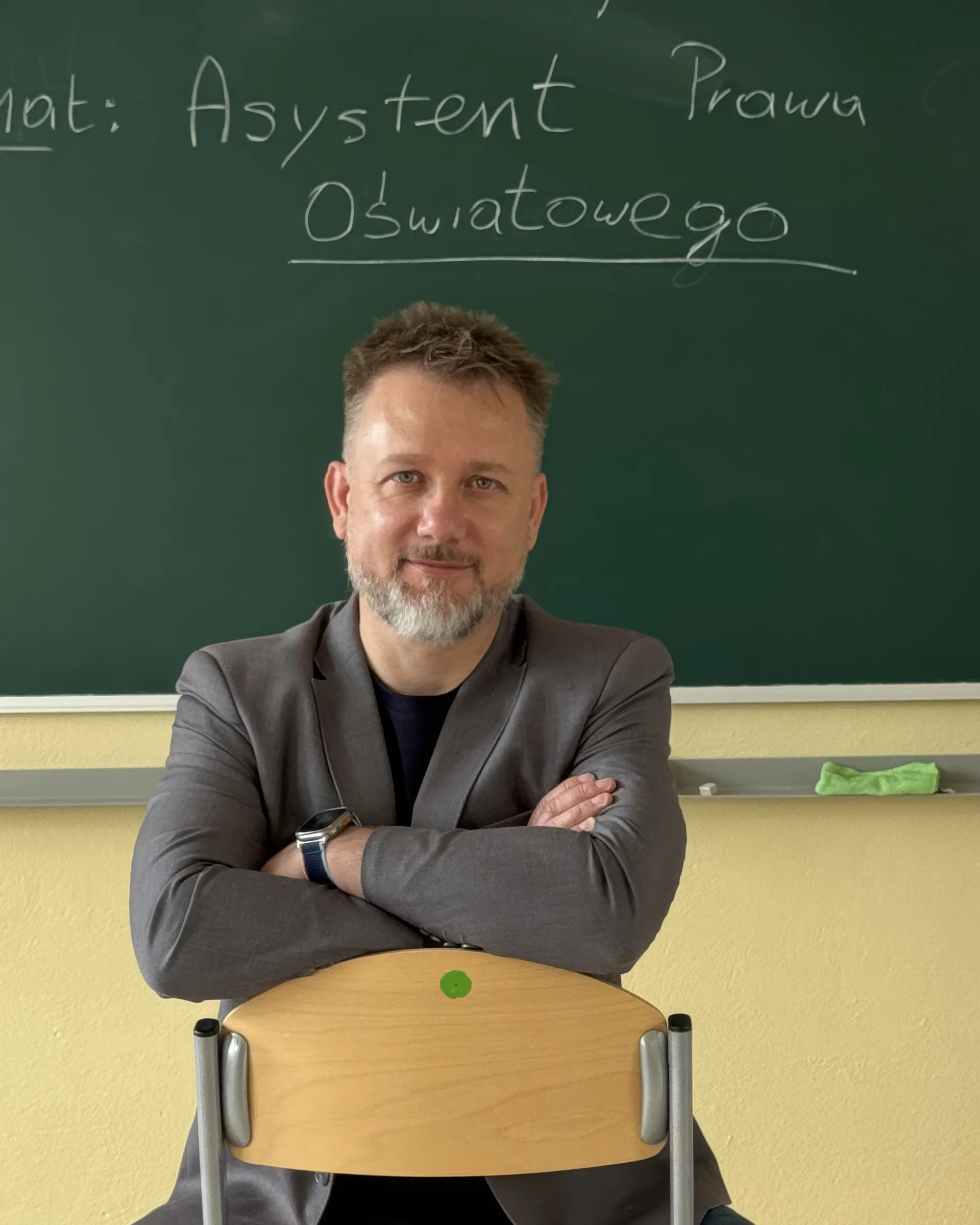 Piotr Kruk w sali lekcyjnej; na tablicy temat: Asystent Prawa Oświatowego