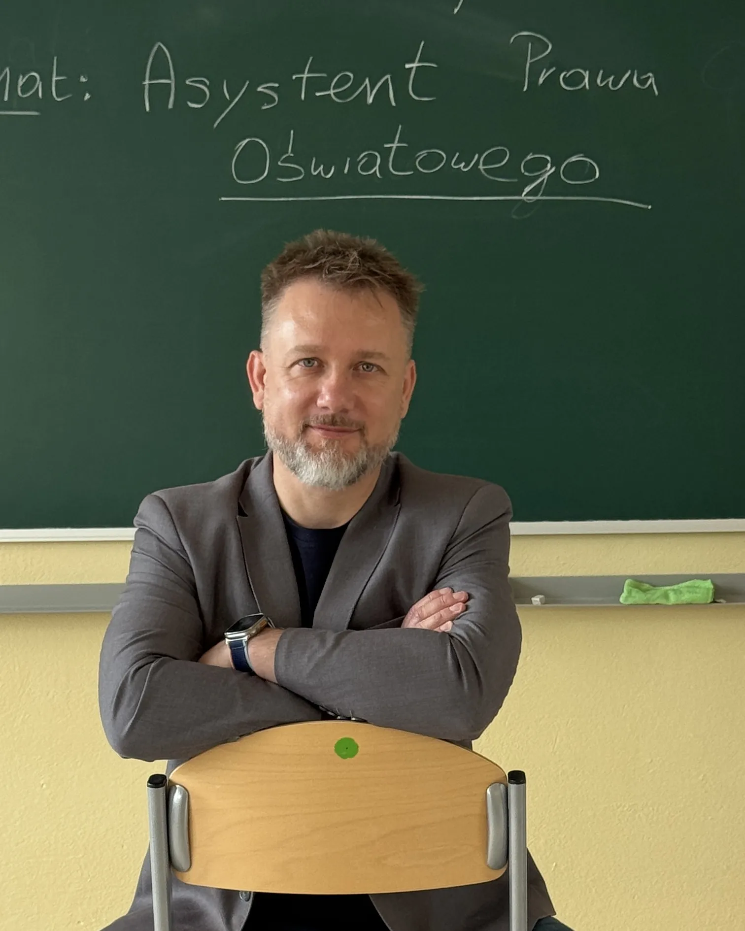 Piotr Kruk w sali lekcyjnej; na tablicy temat: Asystent Prawa Oświatowego