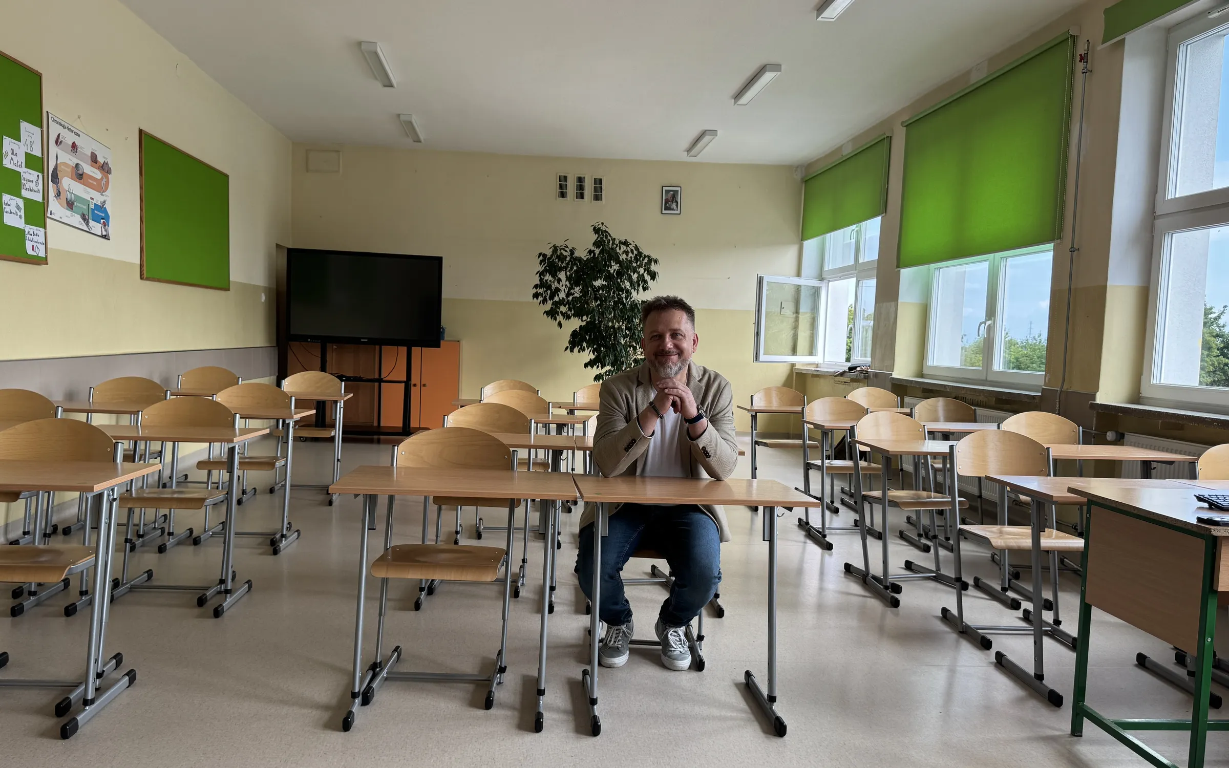 Piotr Kruk siedzi przy szkolnej ławce w pustej sali lekcyjnej