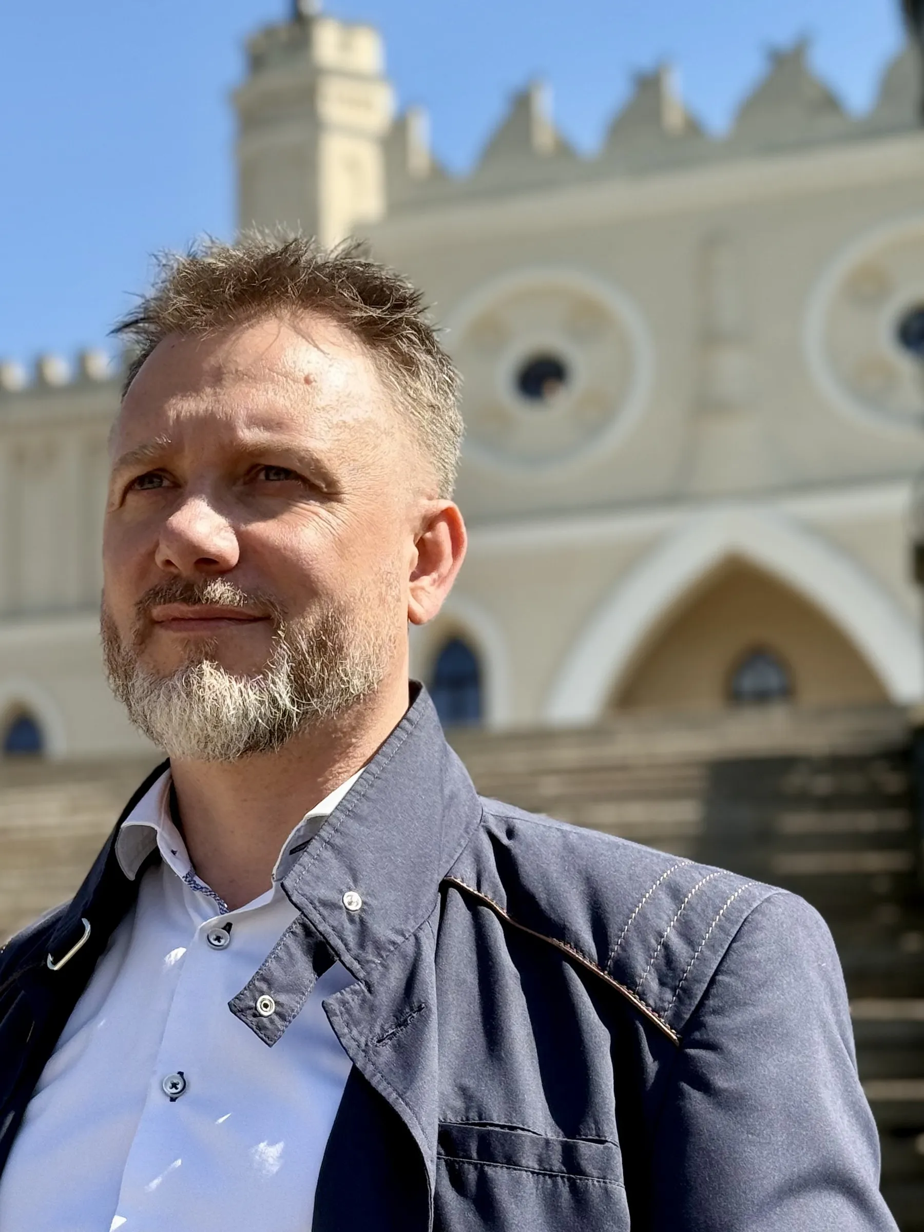 Piotr Kruk — portret w plenerze; w tle zabytkowa kamienica z attyką