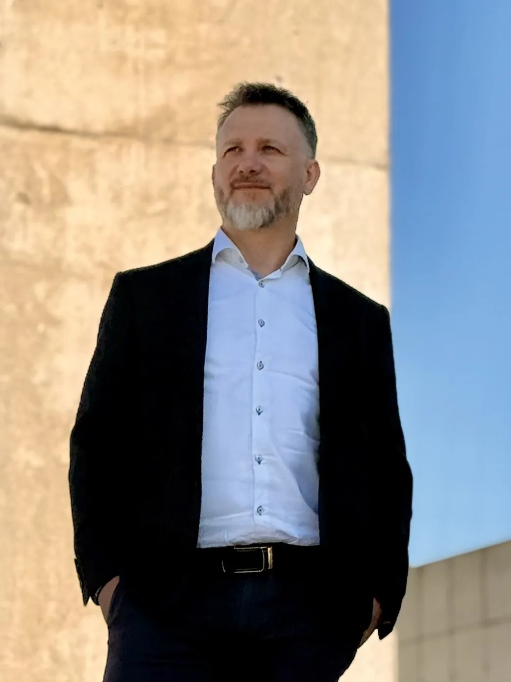 Piotr Kruk — portret całej sylwetki na tle jasnej ściany i nieba