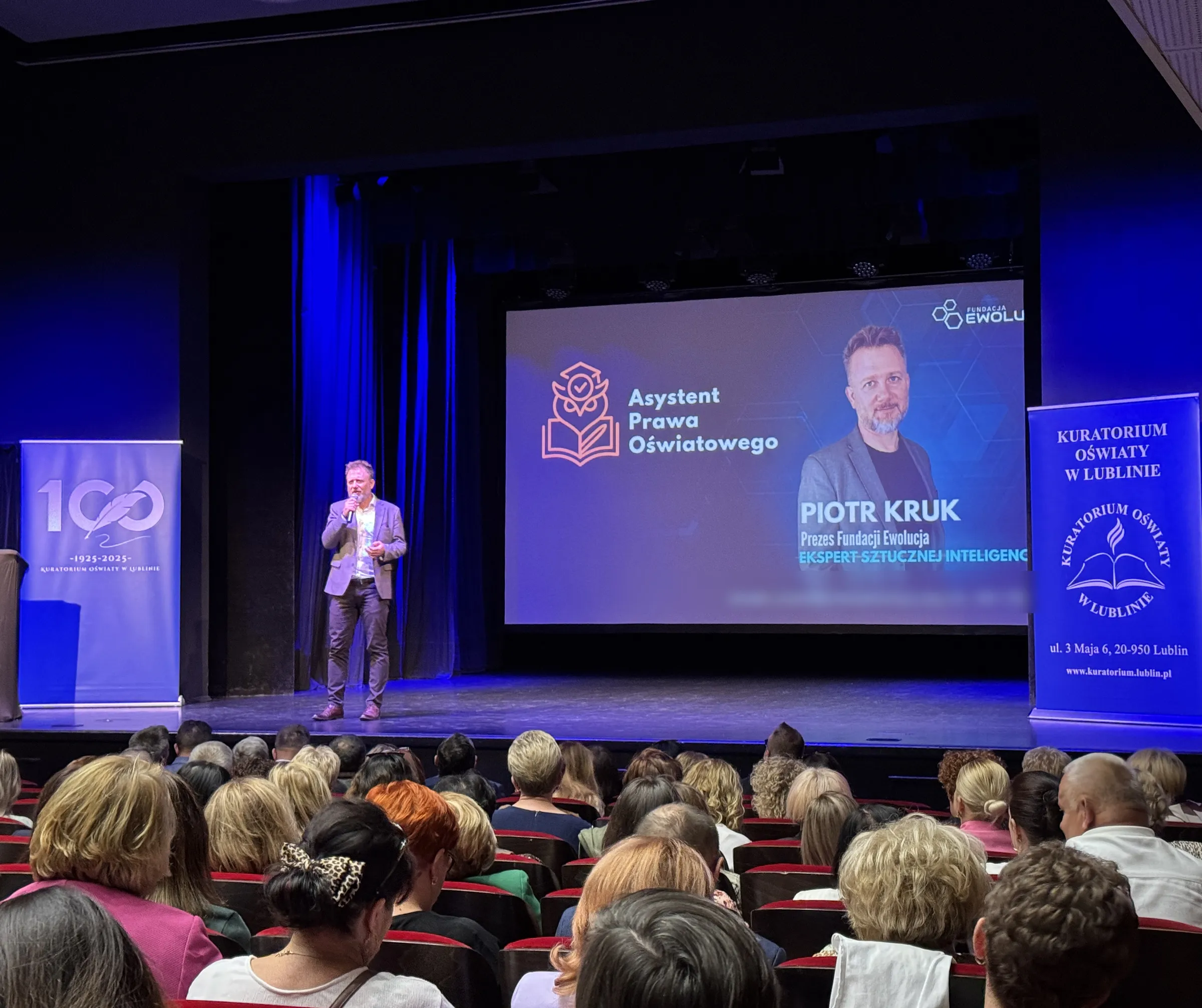 Piotr Kruk na scenie podczas inauguracji roku szkolnego; na ekranie Asystent Prawa Oświatowego