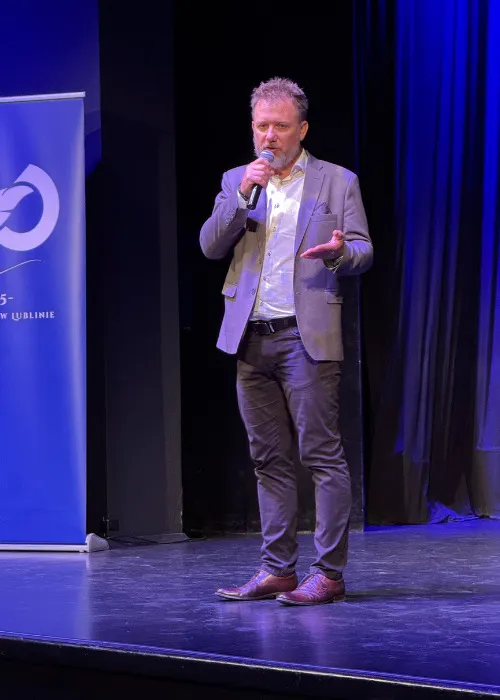 Piotr Kruk przemawia na scenie z mikrofonem; w tle baner konferencyjny