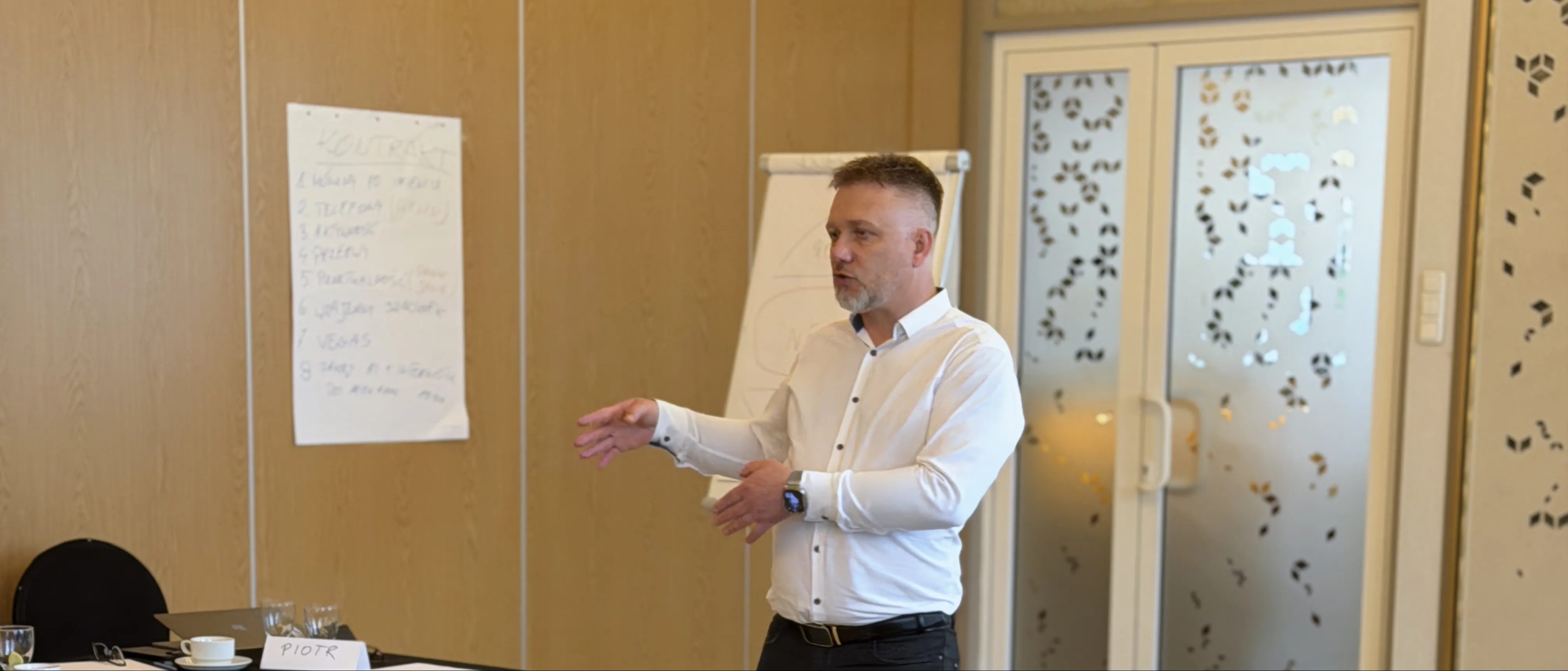 Piotr Kruk prowadzi warsztat — sala szkoleniowa, uczestnicy przy stołach, flipchart z notatkami