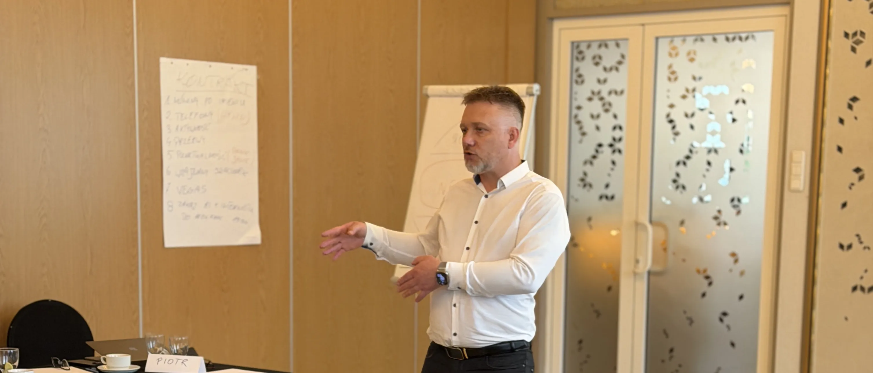 Piotr Kruk prowadzi warsztat — sala szkoleniowa, uczestnicy przy stołach, flipchart z notatkami