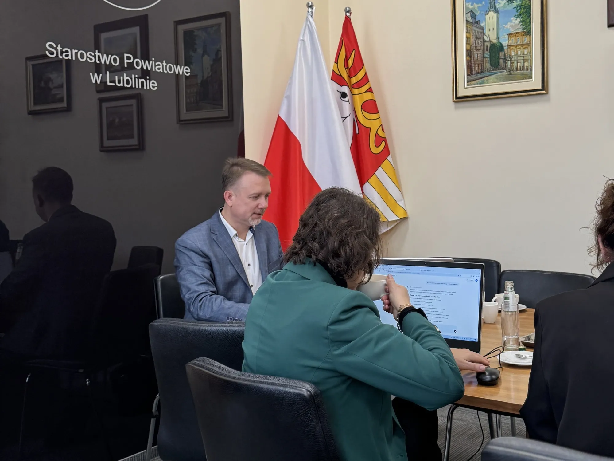 Narada w Starostwie Powiatowym w Lublinie — uczestniczka pracuje z asystentem AI na laptopie, Piotr Kruk rozmawia z zespołem