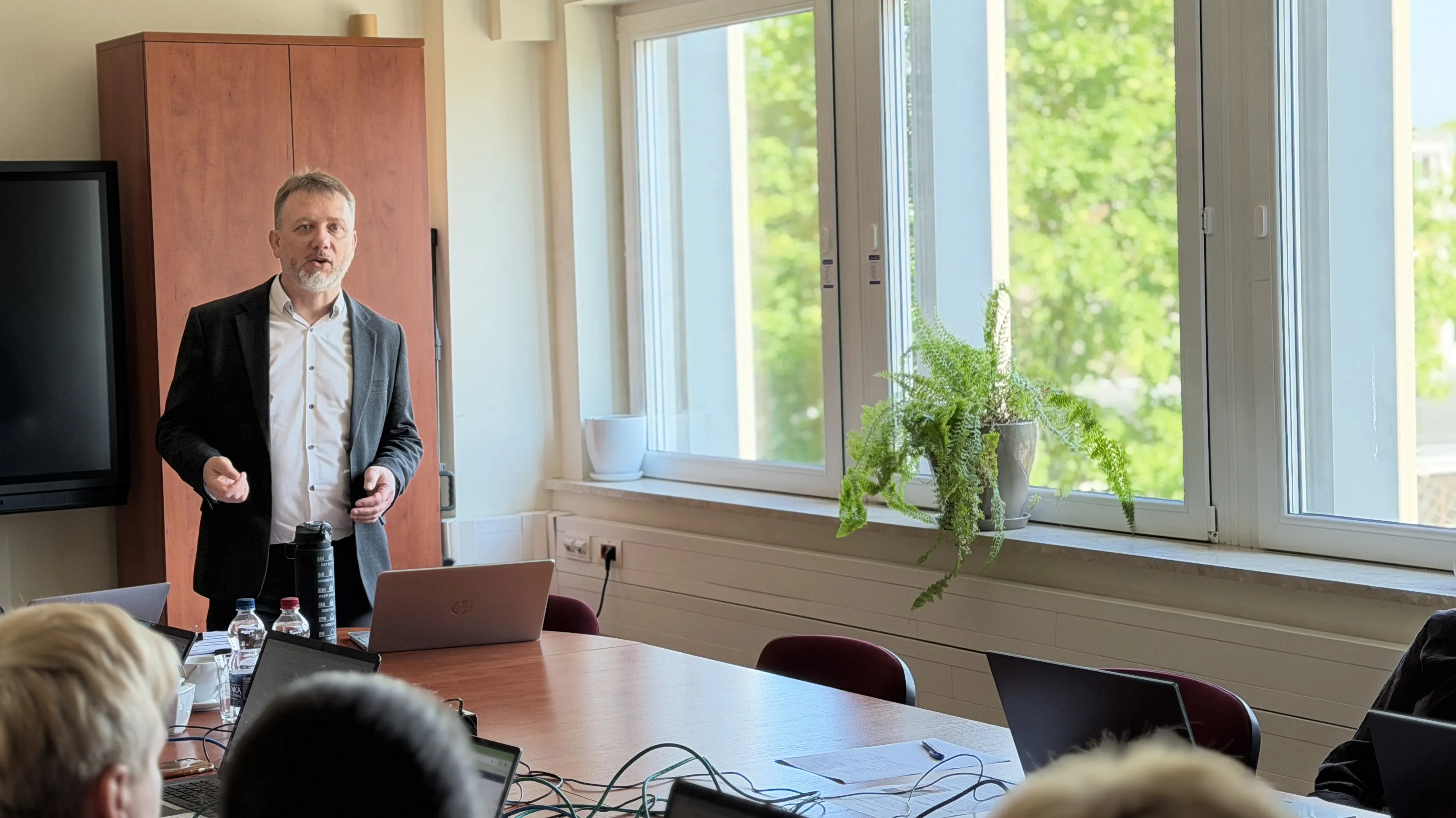 Prowadzący mówi do nauczycieli siedzących z otwartymi laptopami przy stole konferencyjnym
