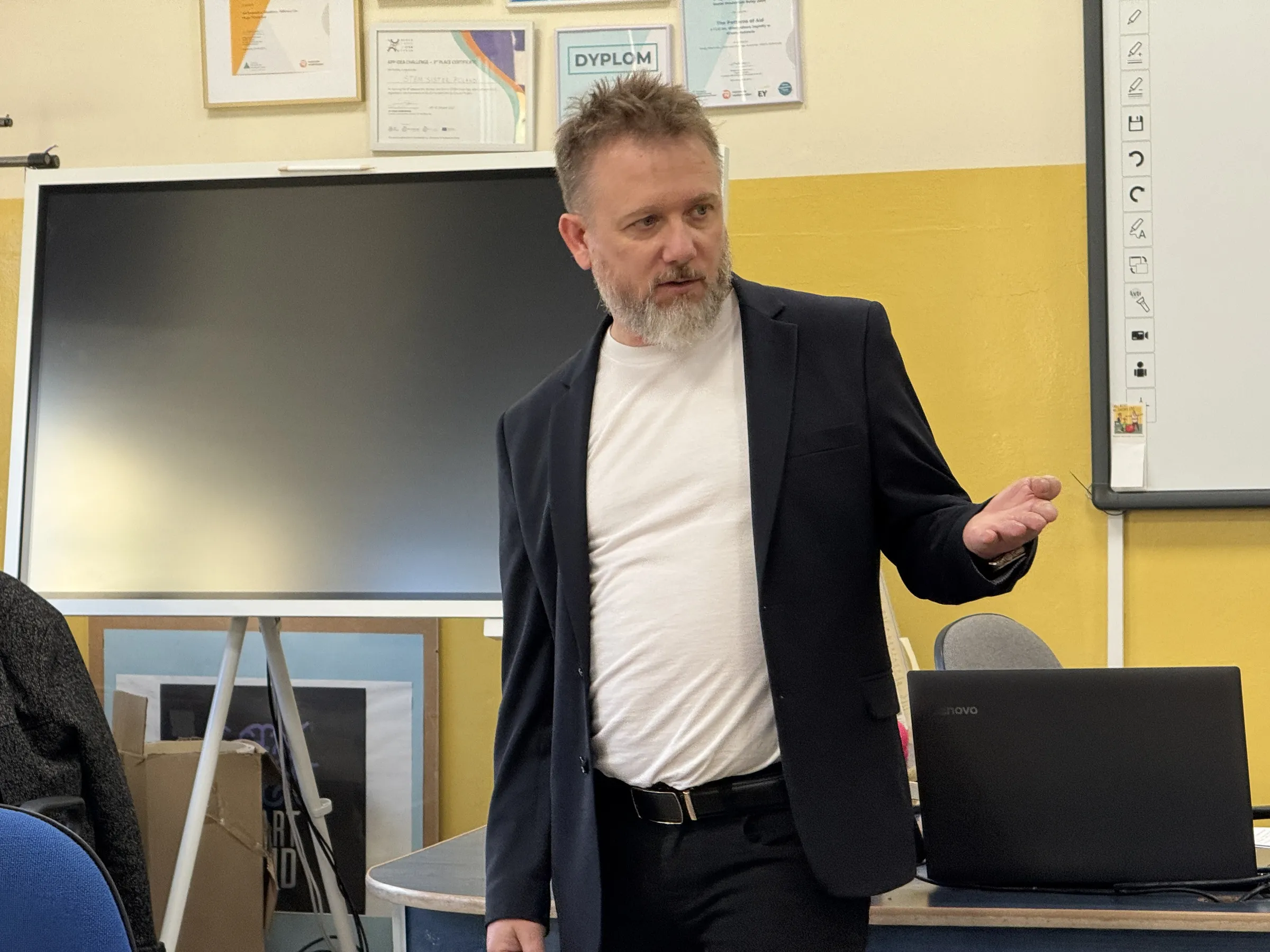Piotr Kruk prowadzi warsztat w szkolnej sali komputerowej — mówi przy tablicy interaktywnej, obok stanowisko z laptopem