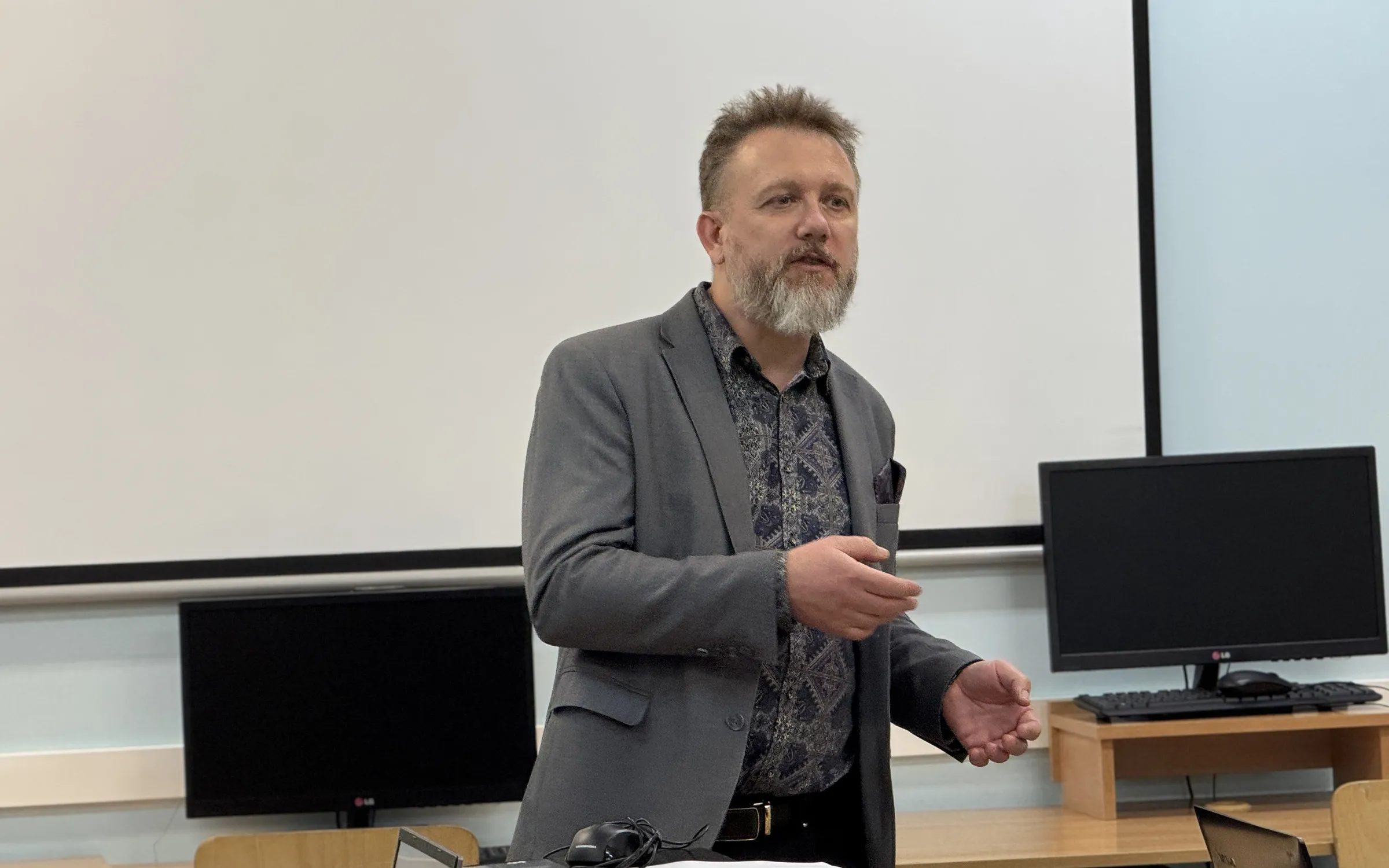 Piotr Kruk tłumaczy zagadnienie prawne w sali szkoleniowej, przy tablicy i stanowiskach komputerowych